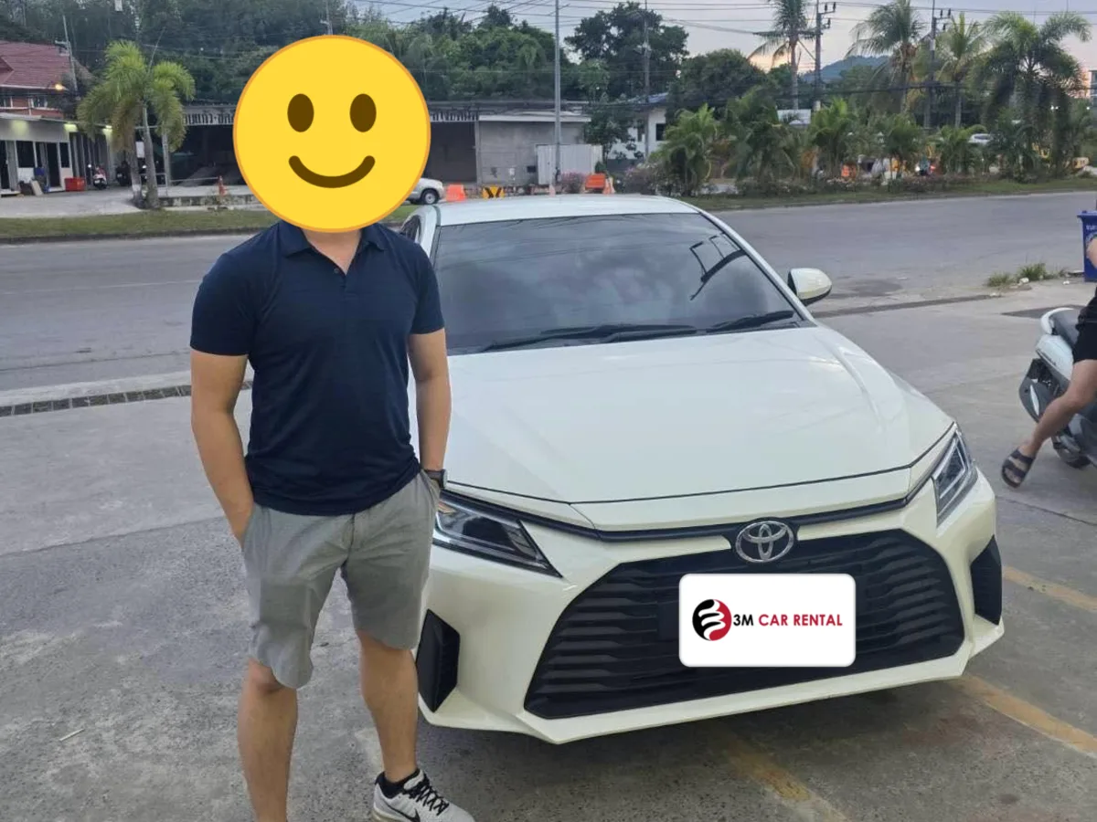 Guest beside a white Toyota Yaris Ativ rental car on a Phuket street