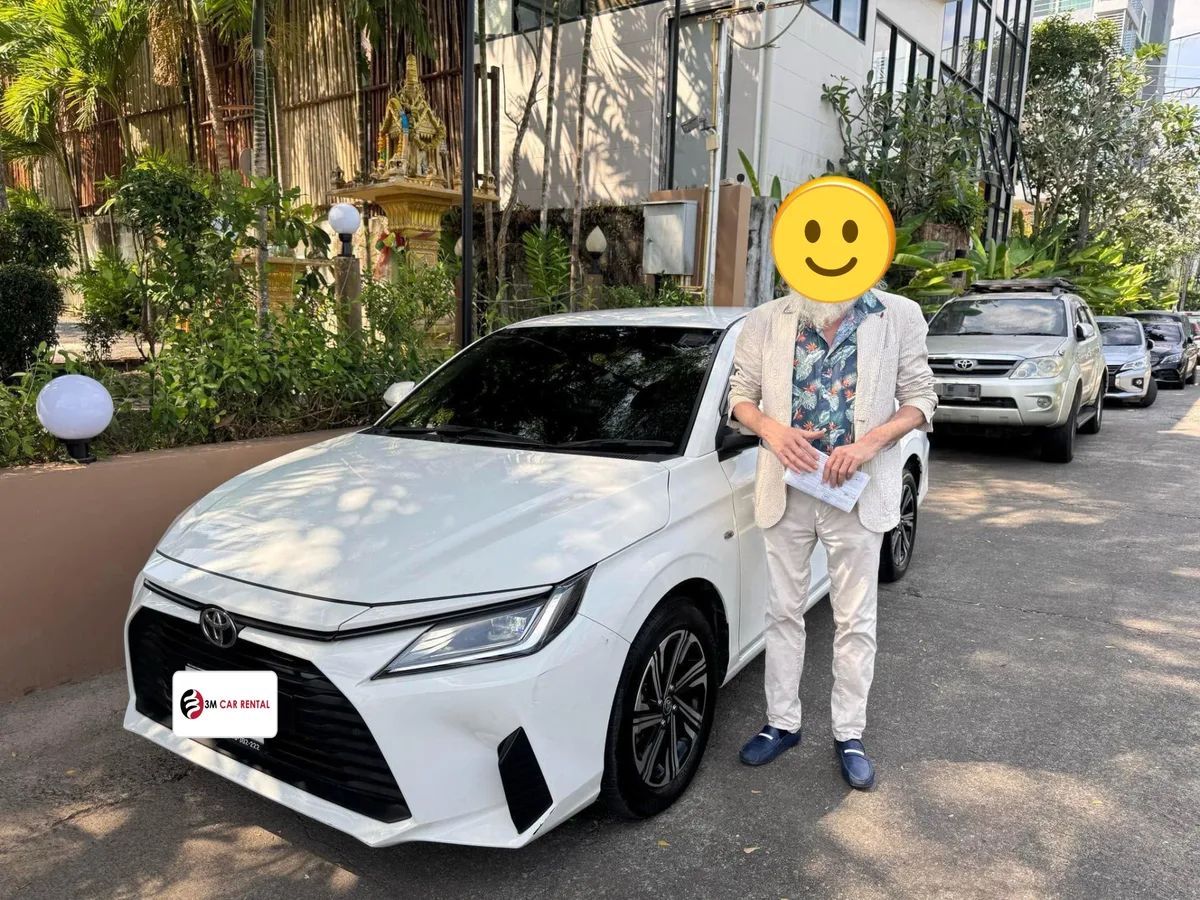 Guest beside a white Toyota sedan rental car in a tropical Phuket garden